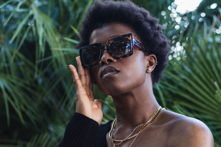 Low angle of serious african american female with afro hairstyle in trendy glasses against palms