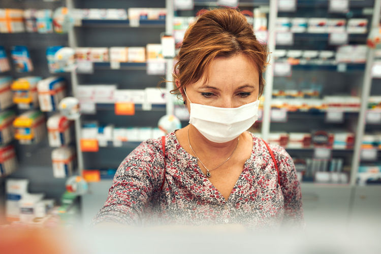 Woman shopping at pharmacy, buying medicines, wearing face mask to cover mouth and nose