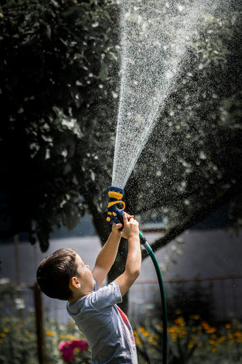Full length of a boy holding water hose water drops childhood play
