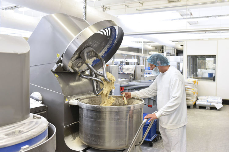 Worker at dough kneading machine in an industrial bakery
