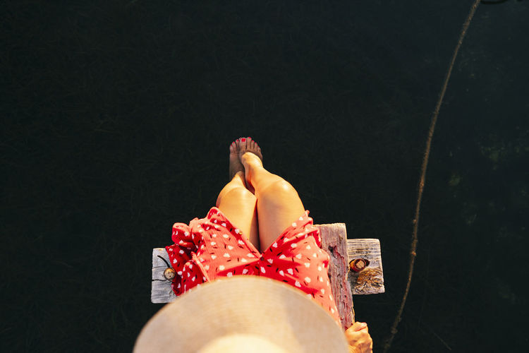 Woman wearing hat sitting with leg in water on edge of pier