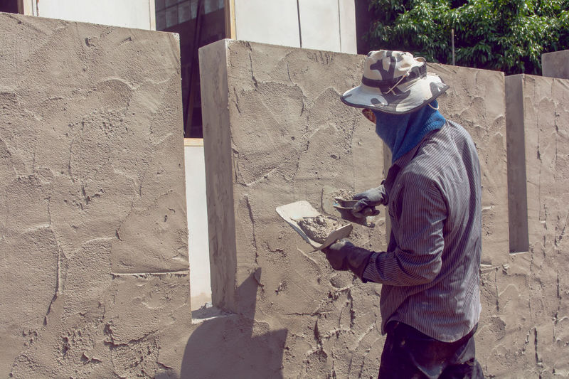 Side view of male plasterer applying cement on wall