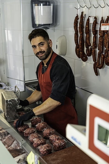 Butcher making raw beef burgers in butchers shop.