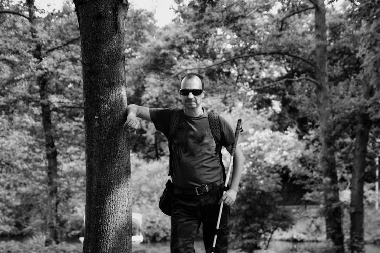 Portrait of man holding pole while standing by tree in forest