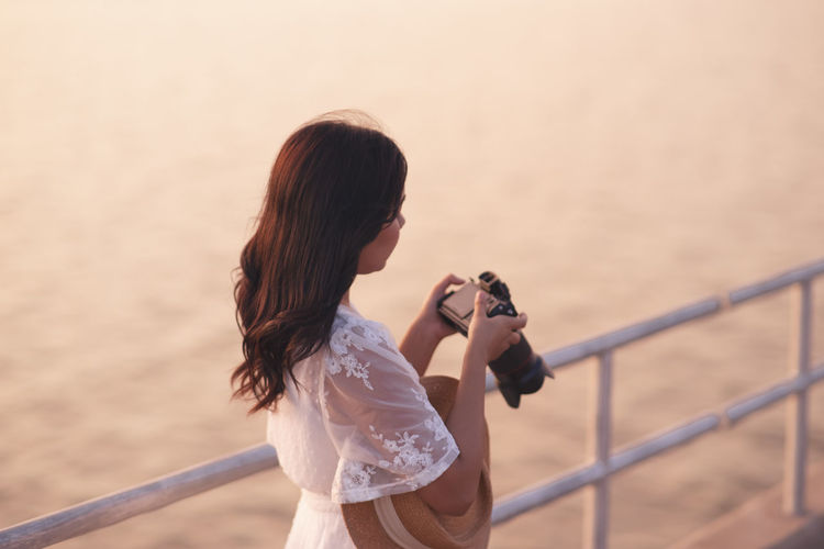 Full length of woman photographing railing against sea