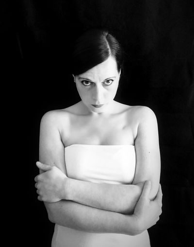 Portrait of young woman with arms crossed standing against black background