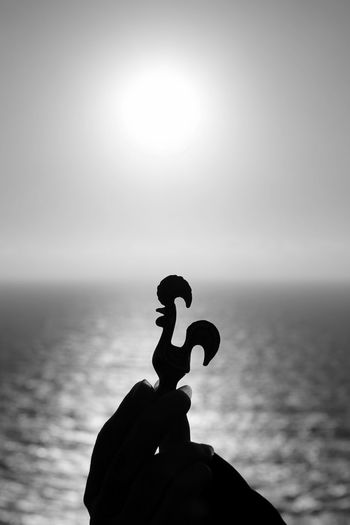 Cropped image of hand holding toy bird by sea against sky