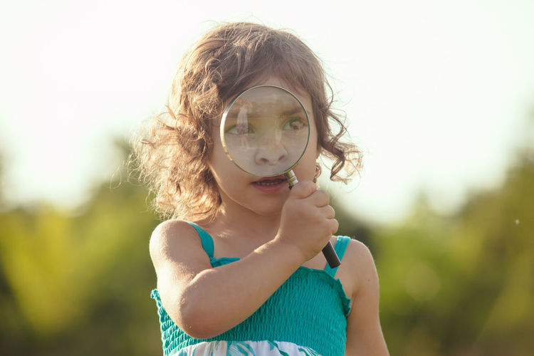 Cute girl holding magnifying glass outdoors
