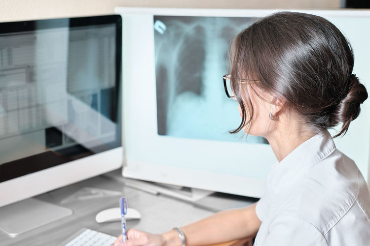 Young asian woman radiologist doctor analysis pulmonary x-ray and make a medical description