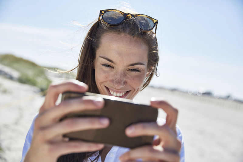 Smiling young woman using cell phone on the beach