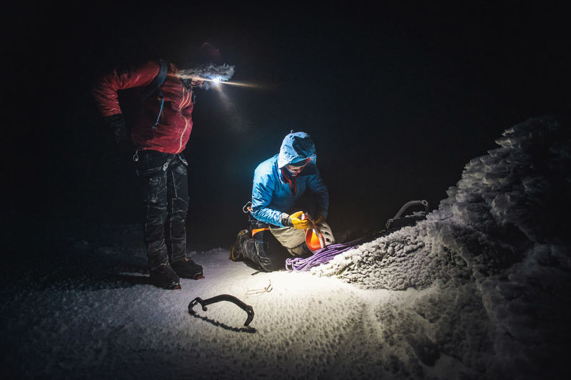 Two alpine climbers sort gear next to an icy cairn in the dark