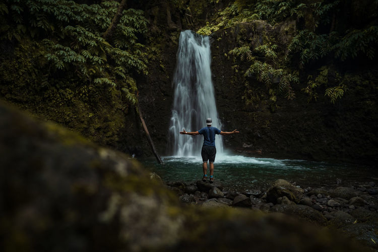 Man standing on rock against waterfall in jungle forest