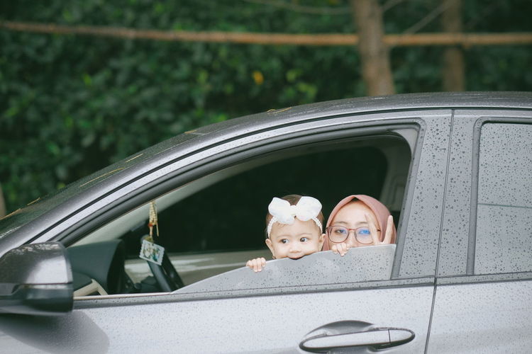A young woman and his baby girl peeking outside car window