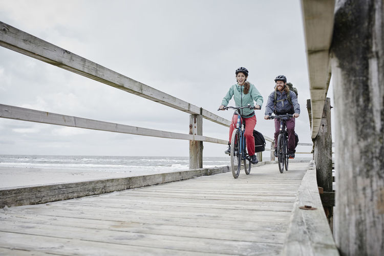 Germany, schleswig-holstein, st peter-ording, couple riding bicycle on jetty at the beach