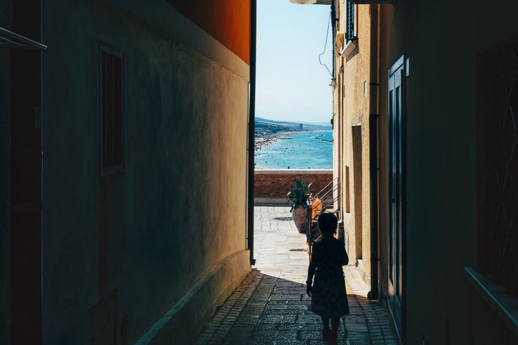 Girl in the shadow of a narrow street looking to the sunny downhill seacoast. last goodbye to summer