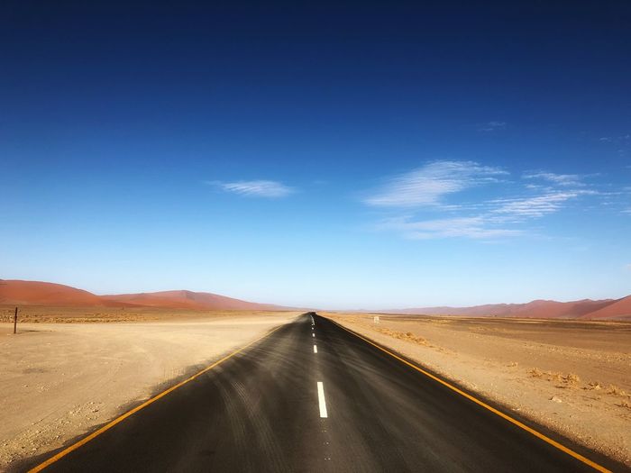 Diminishing perspective of road passing through desert against sky during sunny day