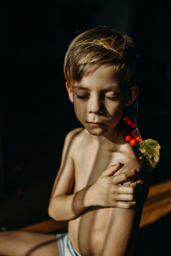 Close-up of shirtless boy with eyes closed sitting at home