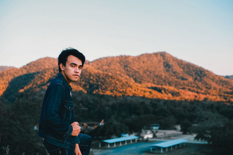 Portrait of young man looking away against mountains