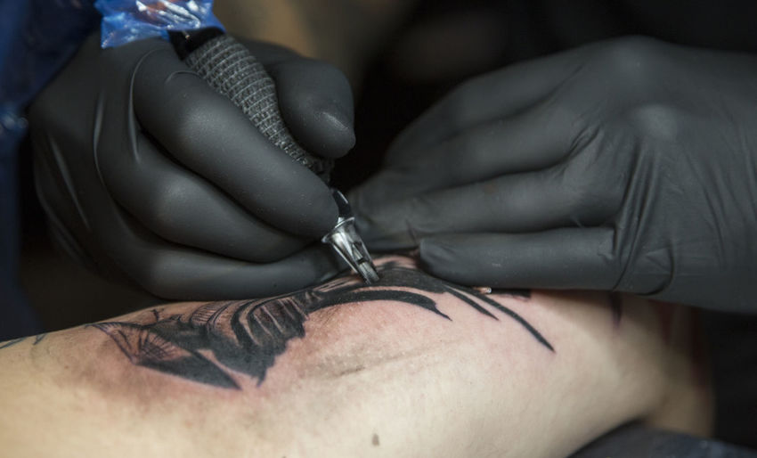 Cropped image of artist making tattoo of man hand