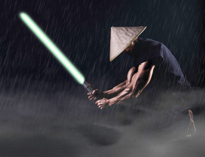 Muscular man holding laser sword against black background