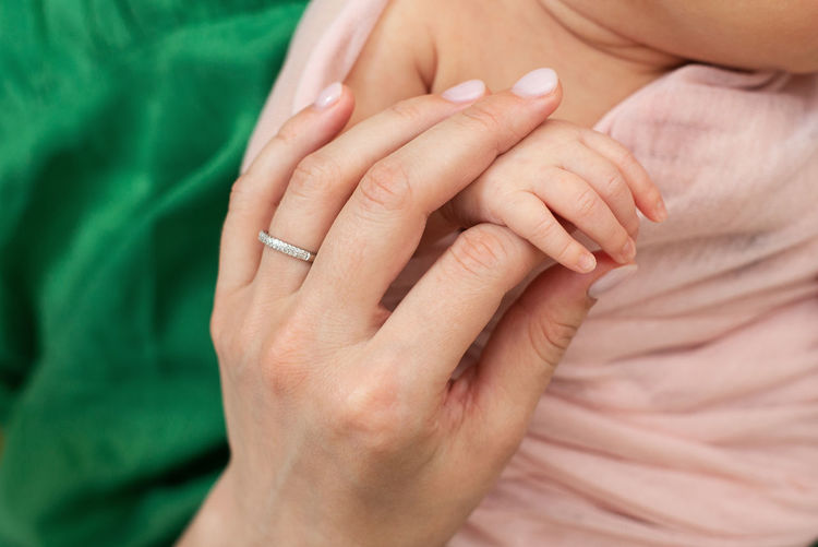 Cropped hand of mother holding baby hand outdoors