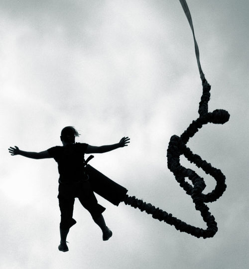 Silhouette man bungee jumping against sky