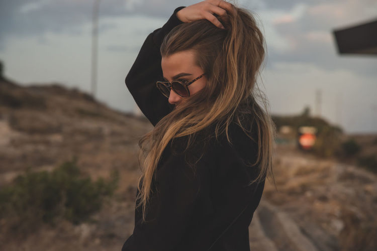 Young woman wearing sunglasses against sky during sunset