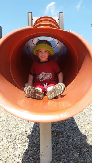 Portrait of boy in slide at playground on sunny day