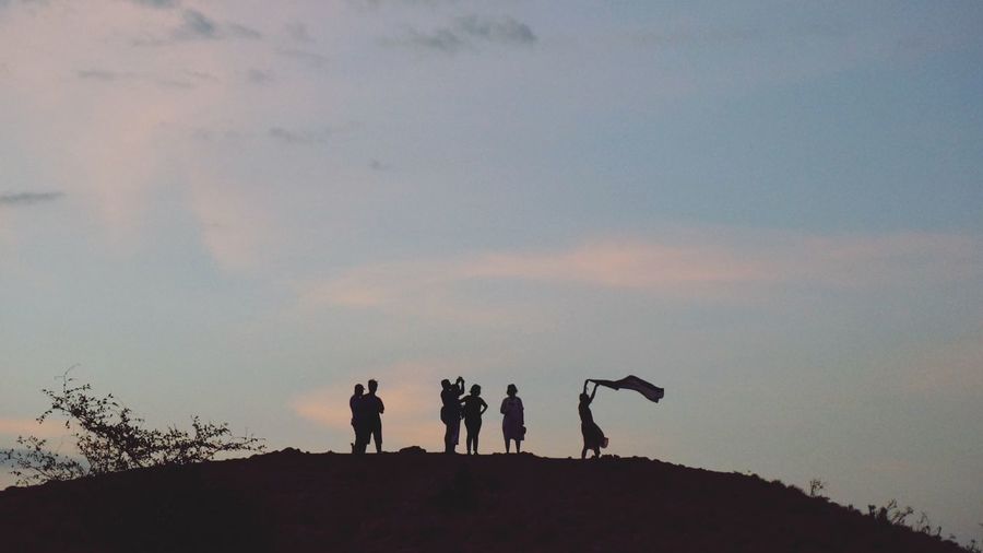 Silhouette people standing on field against sky during sunset