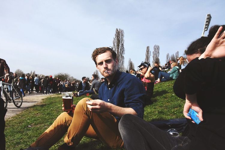 Portrait of man smoking cigarette while sitting with people on grassy field