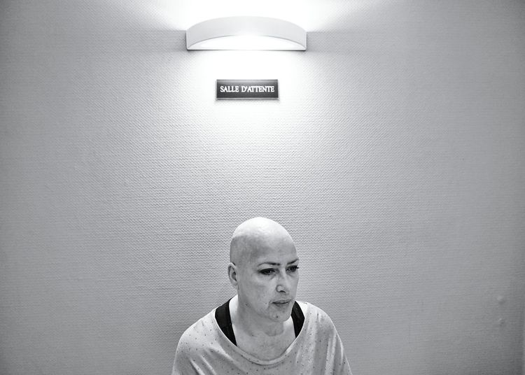 Shaved head woman sitting against illuminated wall at hospital