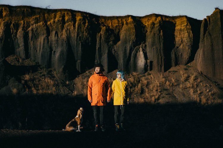 Full length of couple with dog standing against rock mountains