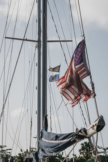 Low angle view of torn american flag waving on boat against sky