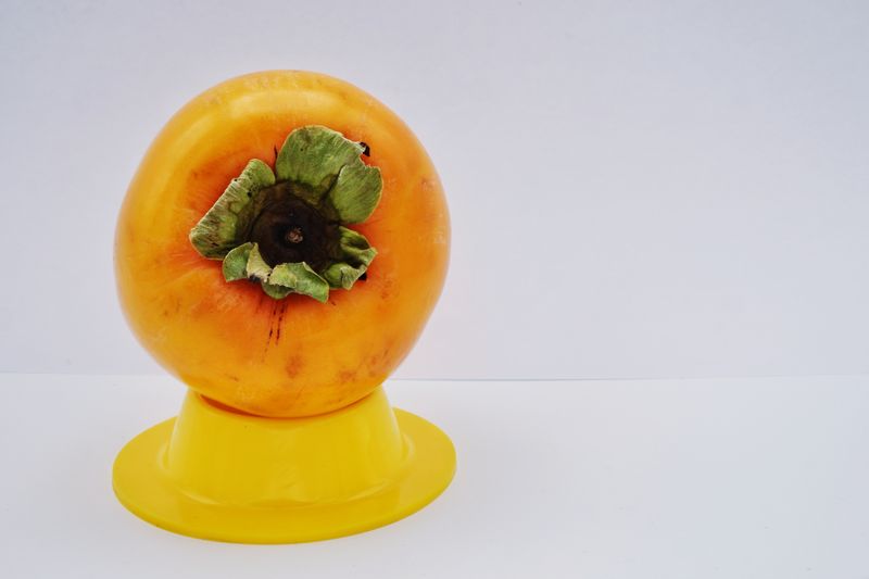 An orange persimmon on top of a yellow silicone egg holder 