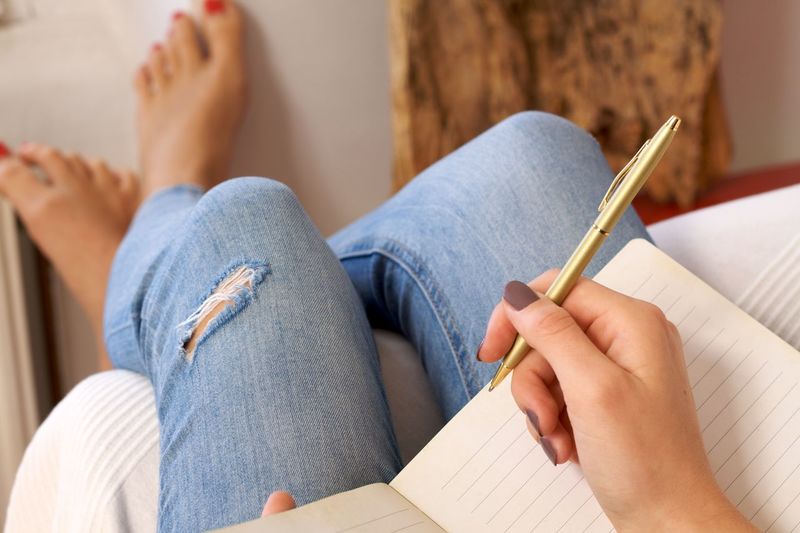 Low section of woman writing in book at home 