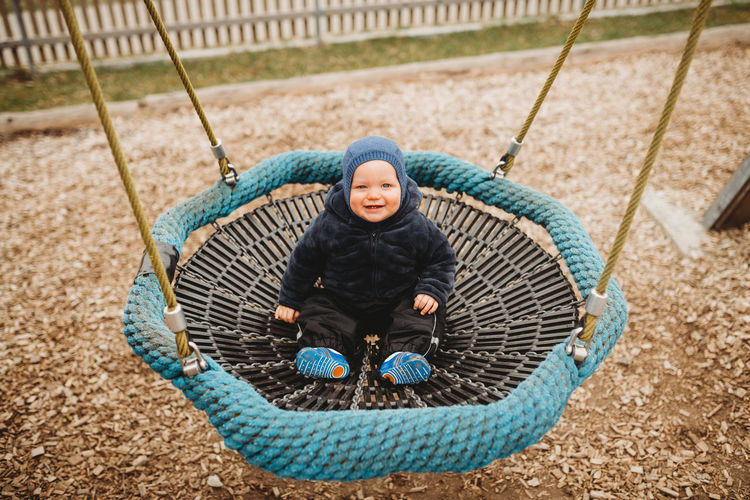 Cute baby in outdoor playground in winter on a nest hammock