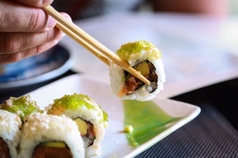 Cropped image of hand holding sushi with chopsticks on table