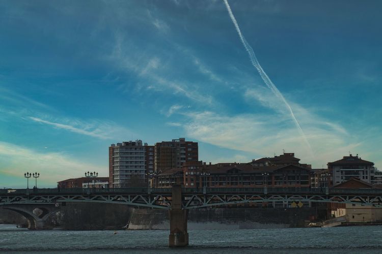 Bridge over river by buildings in city against sky