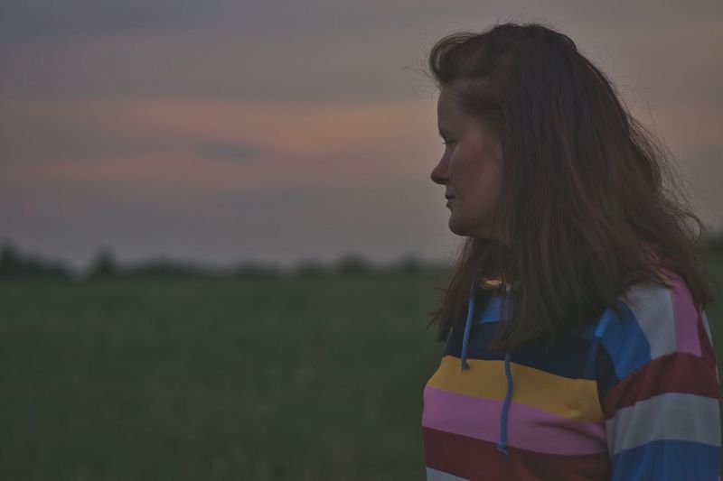 Woman looking away while standing on land against sky during sunset