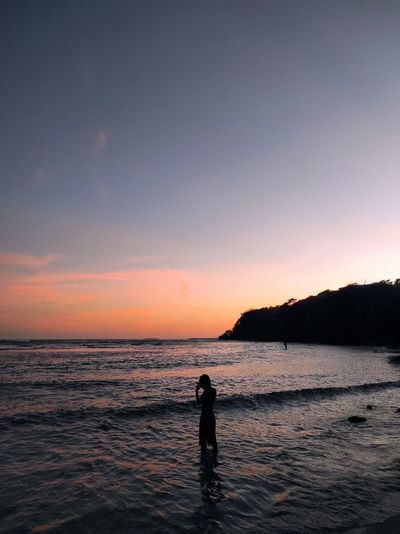 Silhouette person standing on beach against sky during sunset in bali