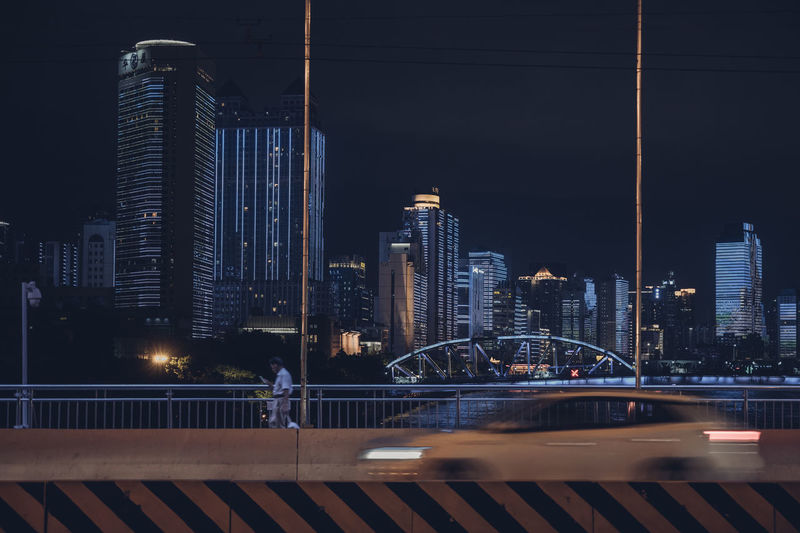 Illuminated bridge and buildings against sky at night