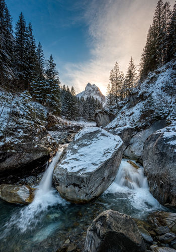 Scenic view of snowcapped stream against sky during winter