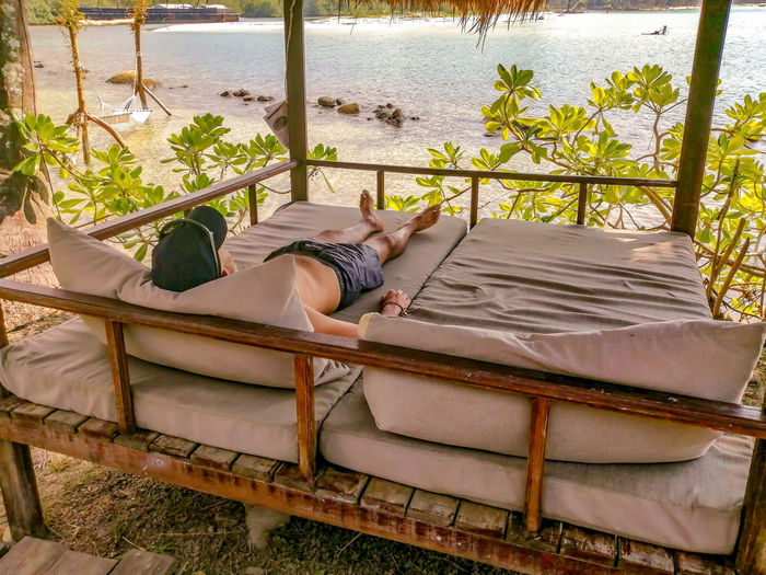 Low section of man sleeping on bed in front of sea, in tropical island 