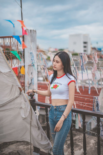Smiling young woman standing against cloudy sky