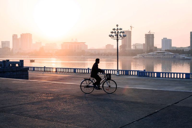 Man riding bicycle on bridge against buildings in city
