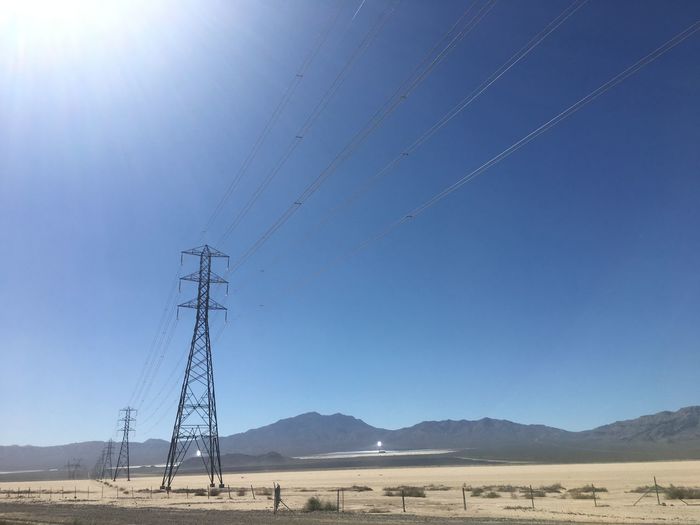 Electricity pylons on landscape against clear blue sky