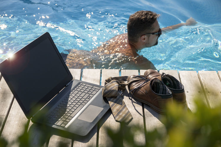 Businessman in swimming pool with personal accessories on wood