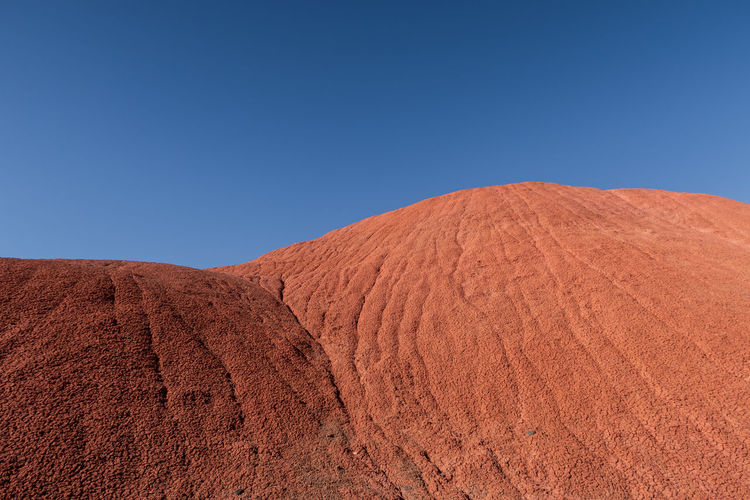 Scenic view of red hills in desert against clear blue sky