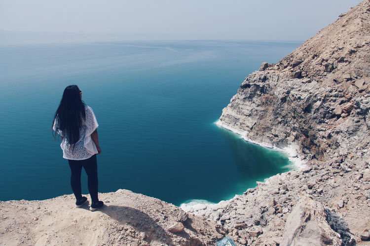 Rear view of girl standing on cliff by the sea
