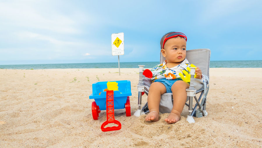 Full length of boy sitting on toy at beach against sky